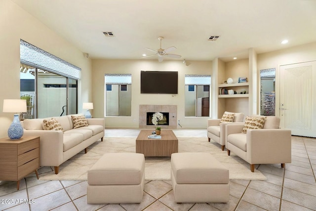 living room with built in shelves, ceiling fan, a tile fireplace, and light tile patterned floors