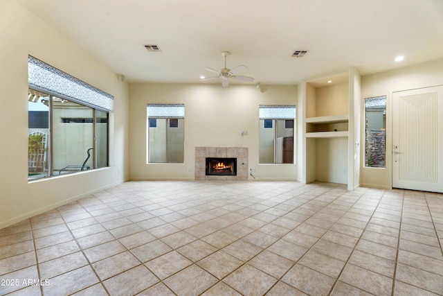 unfurnished living room featuring a tiled fireplace, light tile patterned floors, built in features, and ceiling fan