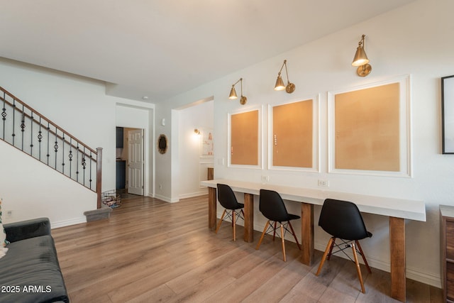 dining space featuring light wood finished floors, stairway, and baseboards