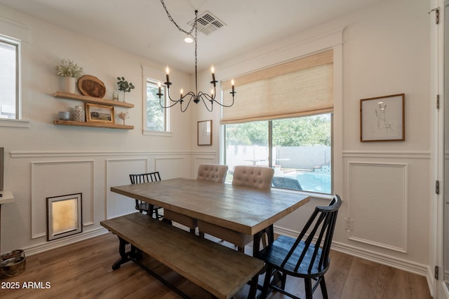 dining area featuring a decorative wall, a chandelier, dark wood-style floors, and wainscoting
