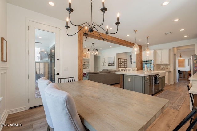 dining room with a chandelier, recessed lighting, light wood-style flooring, and beamed ceiling
