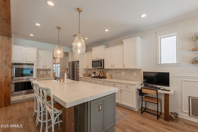kitchen featuring stainless steel appliances, white cabinetry, backsplash, a kitchen bar, and an island with sink