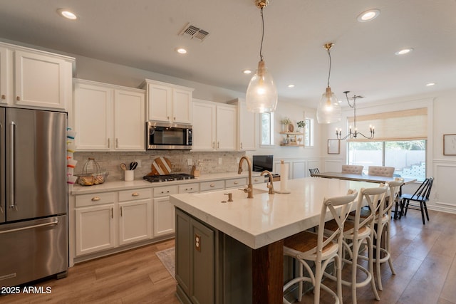 kitchen featuring appliances with stainless steel finishes, white cabinets, light countertops, an island with sink, and wood finished floors
