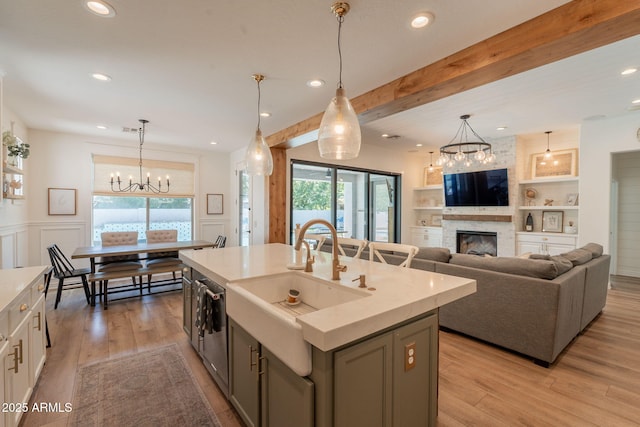 kitchen featuring a chandelier, a sink, beamed ceiling, a large fireplace, and light wood-style floors