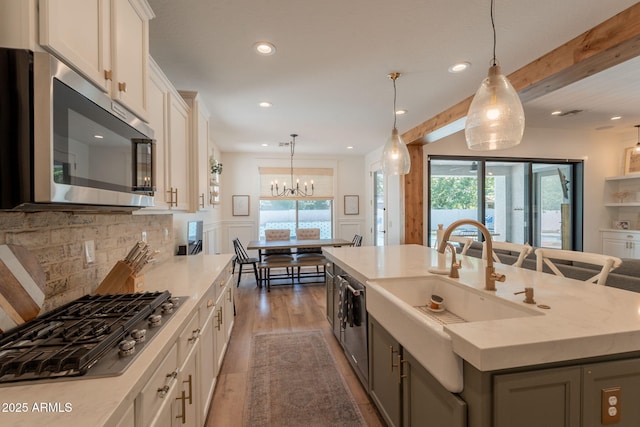 kitchen featuring appliances with stainless steel finishes, a sink, a center island with sink, a chandelier, and light countertops