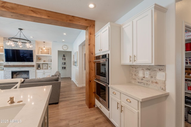 kitchen featuring double oven, light wood finished floors, white cabinetry, open floor plan, and decorative backsplash