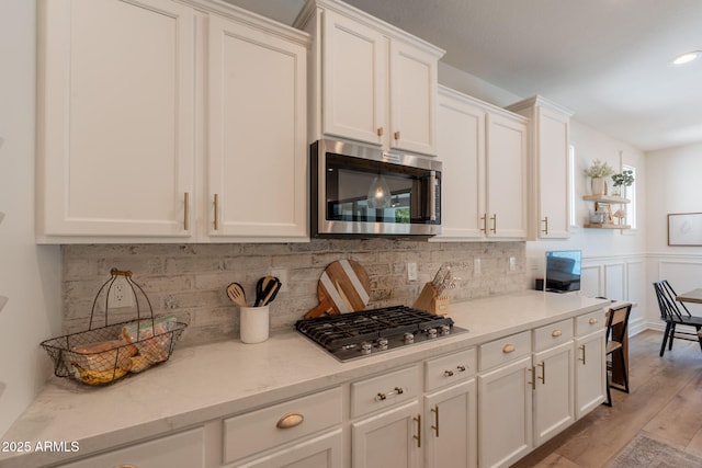 kitchen with appliances with stainless steel finishes, decorative backsplash, white cabinets, light wood-type flooring, and light stone countertops
