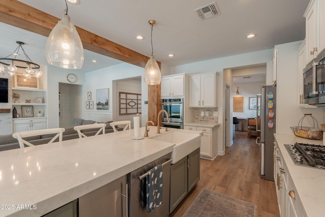 kitchen featuring appliances with stainless steel finishes, open floor plan, wood finished floors, white cabinetry, and beamed ceiling