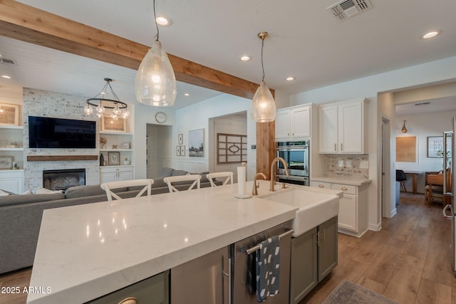 kitchen with open floor plan, beam ceiling, light wood-type flooring, a sink, and light stone countertops