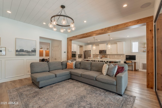 living room with light wood finished floors, a chandelier, wainscoting, a decorative wall, and recessed lighting