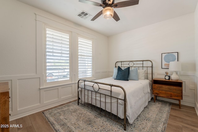 bedroom with a decorative wall, wood finished floors, a wainscoted wall, and a ceiling fan