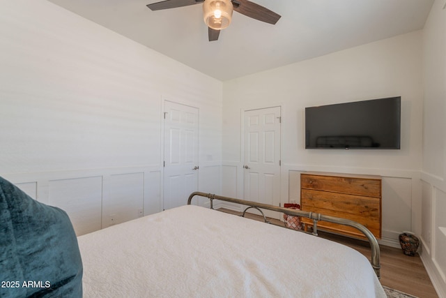 bedroom featuring wood finished floors, a wainscoted wall, ceiling fan, and a decorative wall