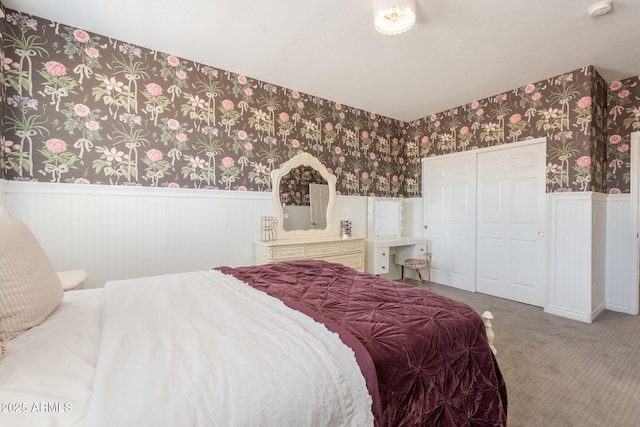 bedroom with wainscoting, wallpapered walls, carpet floors, and a closet