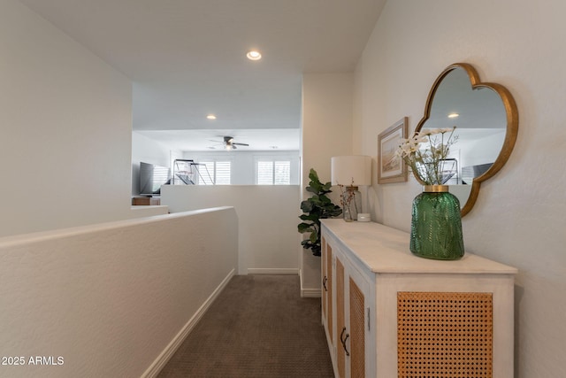 corridor featuring dark colored carpet, recessed lighting, baseboards, and an upstairs landing
