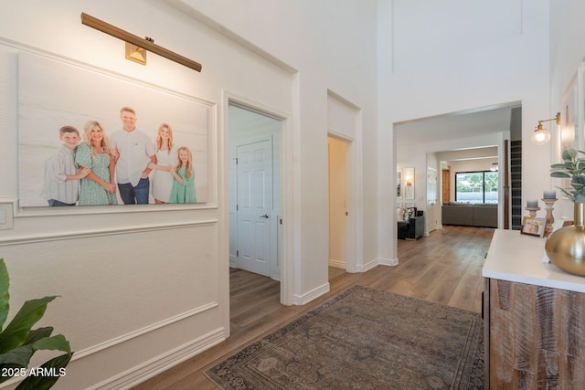 hall featuring wood finished floors, baseboards, and a high ceiling