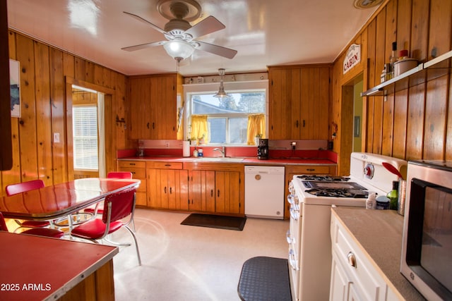 kitchen with ceiling fan, white appliances, wooden walls, and a sink