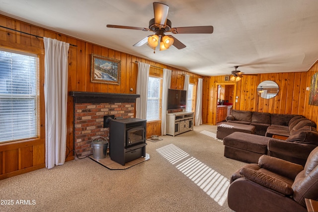 living room featuring light carpet, wood walls, a wood stove, and ceiling fan