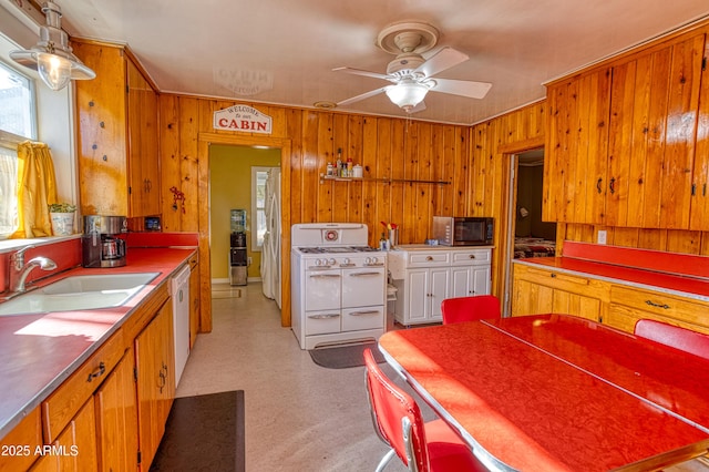 kitchen with a ceiling fan, a sink, white appliances, wooden walls, and light floors