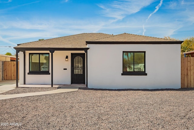 view of front of home featuring a shingled roof, fence, and stucco siding