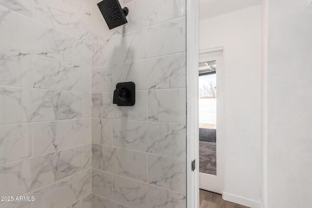 full bathroom with a tile shower, baseboards, and wood finished floors