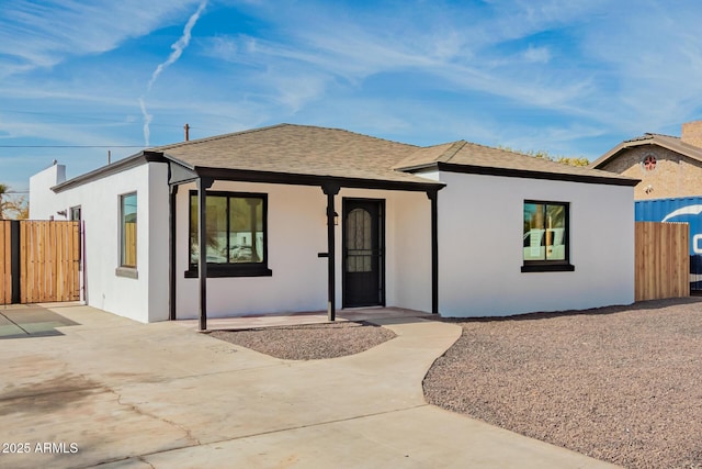 view of front of home featuring a shingled roof, fence, a patio, and stucco siding