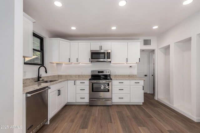 kitchen with sink, white cabinetry, light stone counters, appliances with stainless steel finishes, and dark hardwood / wood-style flooring