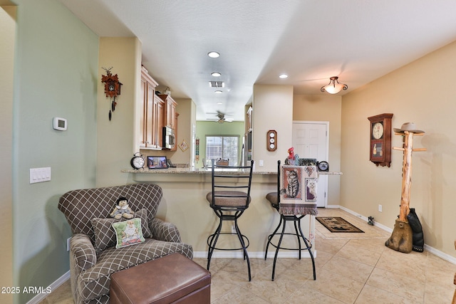 kitchen with baseboards, visible vents, stainless steel microwave, a peninsula, and a kitchen bar