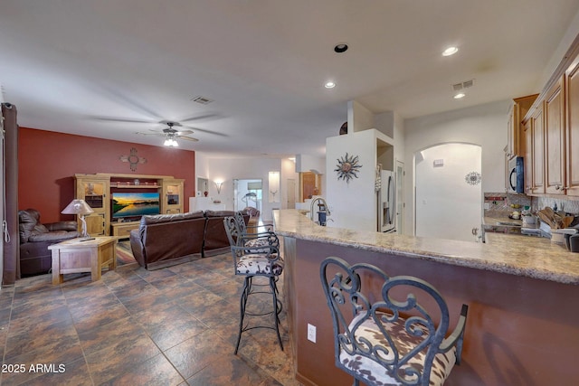 kitchen featuring kitchen peninsula, stainless steel refrigerator with ice dispenser, ceiling fan, sink, and a breakfast bar area