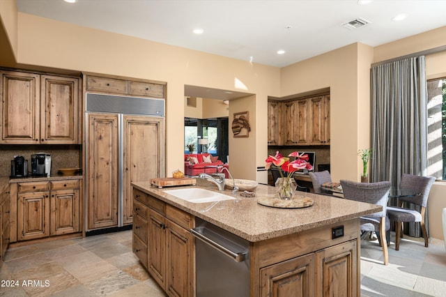 kitchen with backsplash, plenty of natural light, sink, and a kitchen island with sink