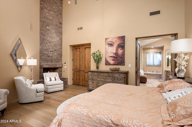 bedroom featuring a fireplace, light wood-type flooring, a high ceiling, and connected bathroom