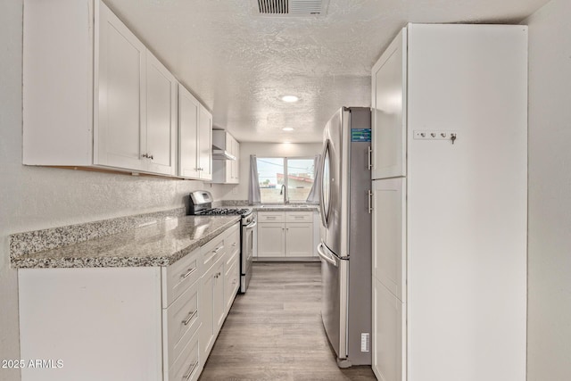 kitchen with appliances with stainless steel finishes, white cabinetry, sink, light stone counters, and a textured ceiling