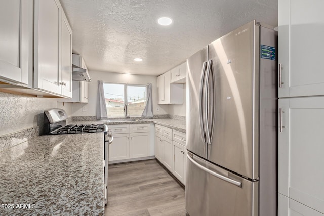 kitchen featuring light stone countertops, a textured ceiling, stainless steel appliances, and white cabinets