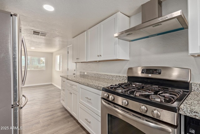 kitchen featuring light stone counters, wall chimney range hood, white cabinets, and appliances with stainless steel finishes