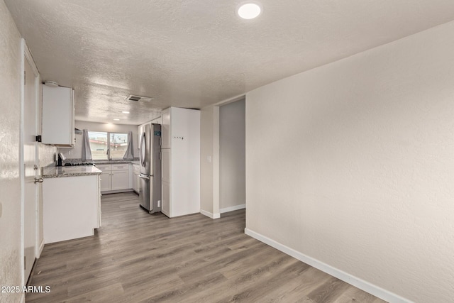 kitchen with hardwood / wood-style floors, stainless steel refrigerator, white cabinets, light stone counters, and a textured ceiling