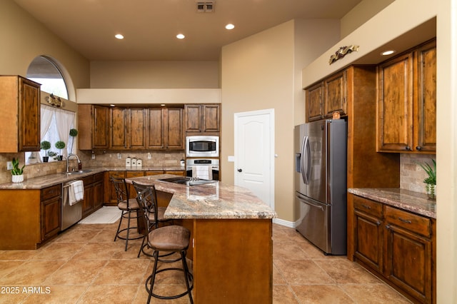 kitchen featuring sink, backsplash, stainless steel appliances, light stone countertops, and a kitchen island