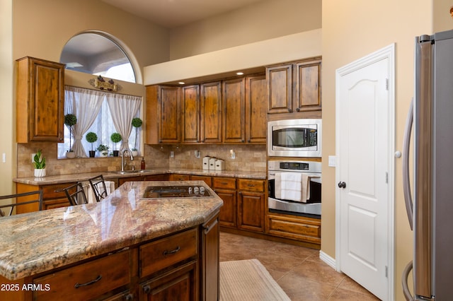 kitchen featuring sink, backsplash, stainless steel appliances, light stone countertops, and a kitchen island