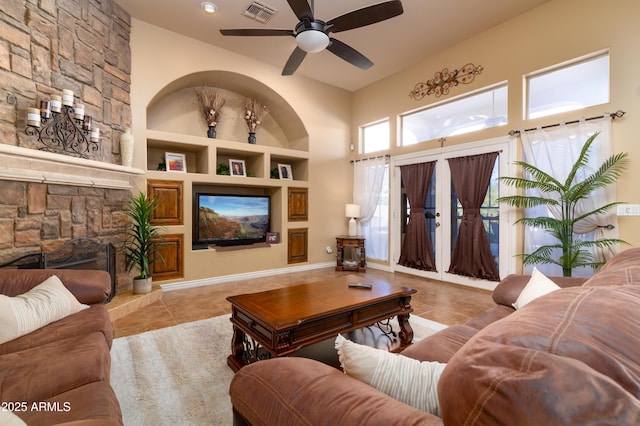 tiled living room with built in shelves, a stone fireplace, and ceiling fan