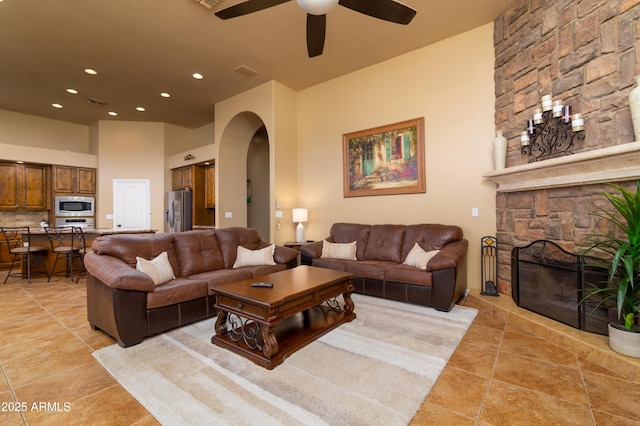 living room featuring a stone fireplace, a towering ceiling, and ceiling fan