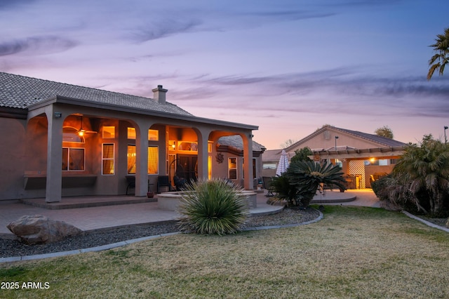 back house at dusk with a patio and a lawn