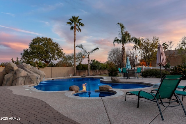 pool at dusk featuring an in ground hot tub and a patio