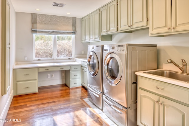 washroom with light hardwood / wood-style floors, sink, washer and clothes dryer, and cabinets