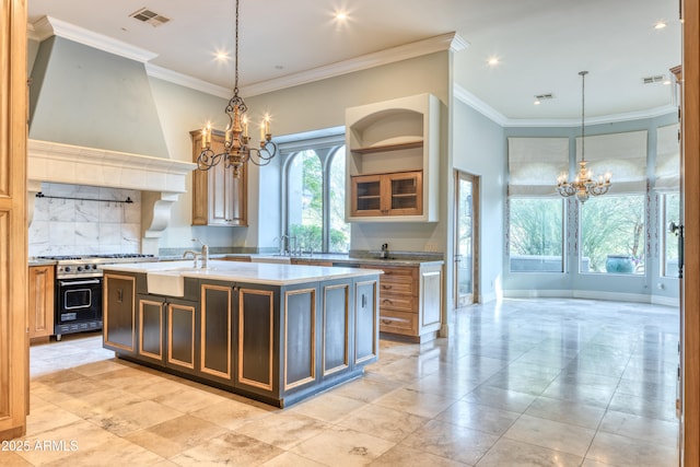 kitchen featuring pendant lighting, custom exhaust hood, stainless steel range, an inviting chandelier, and a kitchen island with sink