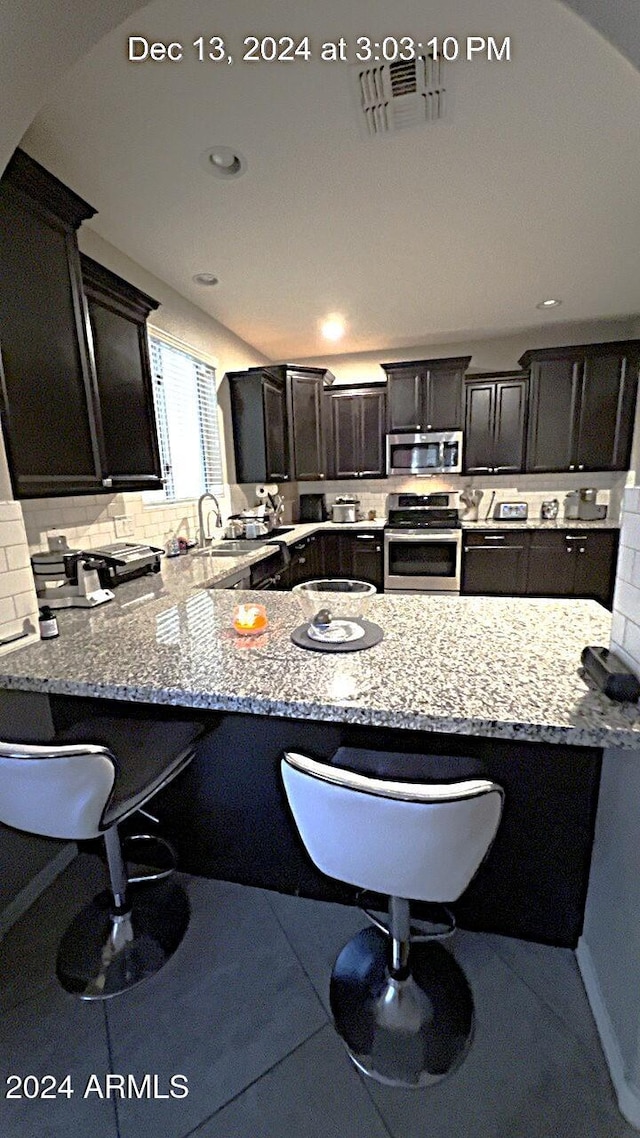 kitchen featuring tasteful backsplash, light stone counters, tile patterned floors, a breakfast bar area, and appliances with stainless steel finishes