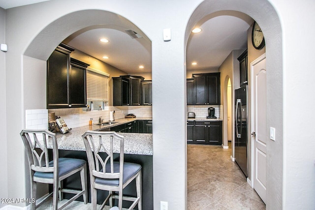 kitchen with sink, a kitchen breakfast bar, light stone counters, stainless steel fridge, and decorative backsplash