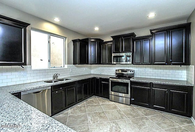 kitchen featuring decorative backsplash, stainless steel appliances, light stone counters, and sink