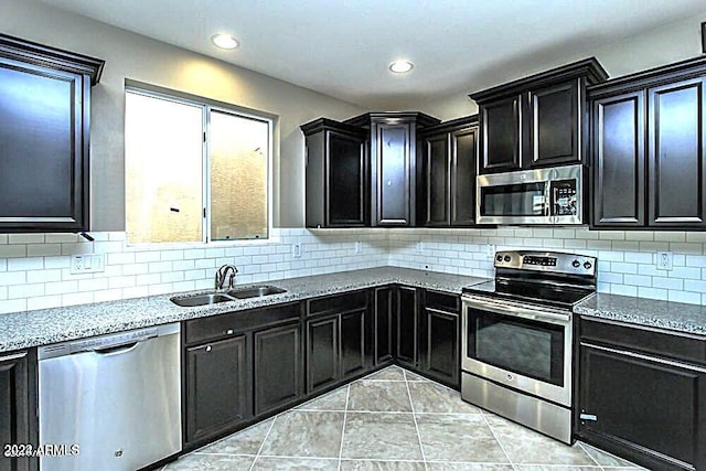 kitchen featuring backsplash, sink, light tile patterned floors, appliances with stainless steel finishes, and light stone counters