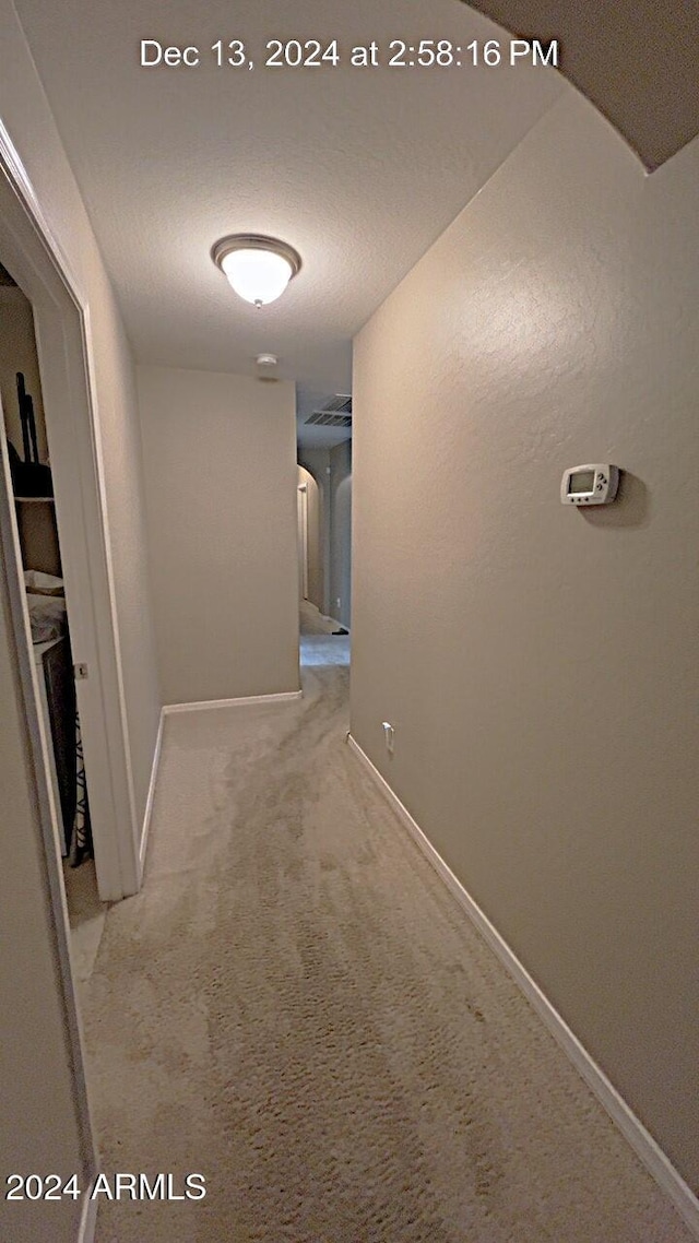 hall with light carpet and a textured ceiling