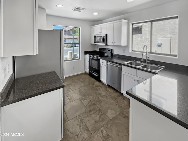 kitchen featuring white cabinets, stainless steel appliances, sink, and dark stone counters