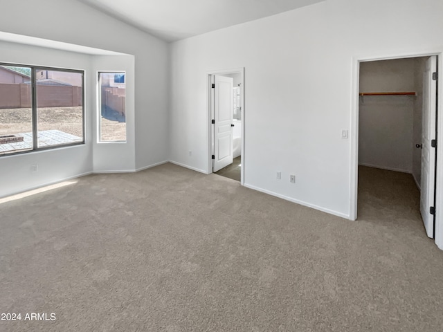 unfurnished bedroom with a walk in closet, vaulted ceiling, a closet, ensuite bath, and light colored carpet