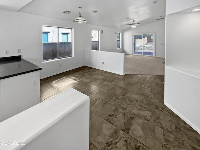 unfurnished living room featuring lofted ceiling, dark colored carpet, ceiling fan, and plenty of natural light